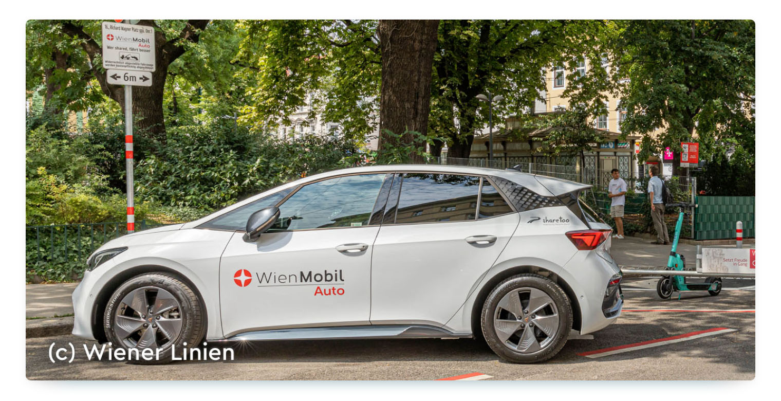 A grey car with the print "WienMobil Auto" stands on a parking space surrounded by trees in Vienna