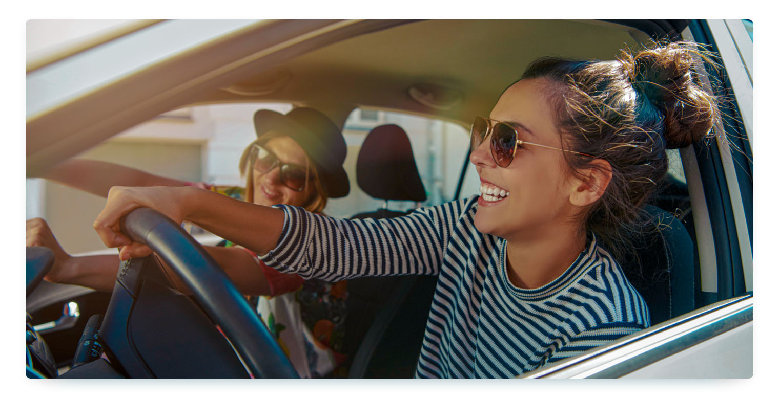 Two young women are driving a car while laughing, being clearly in a good mood