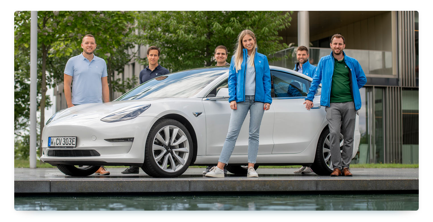 Team members of carvaloo standing around a grey vehicle in front of a water pool