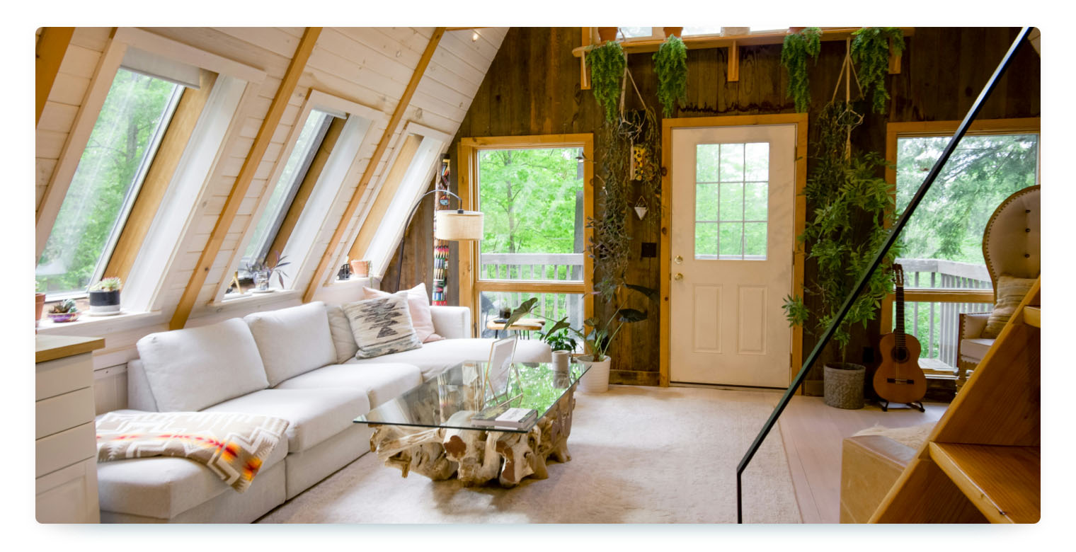 A cozy Airbnb home with white wood walls, a white couch, many plants and views into nature