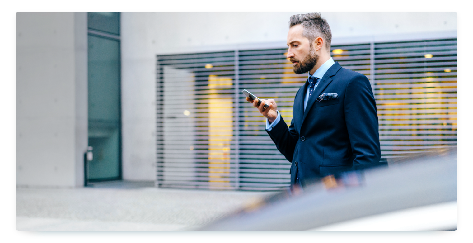 A buisnessman walking towards a car with his smartphone in his hand