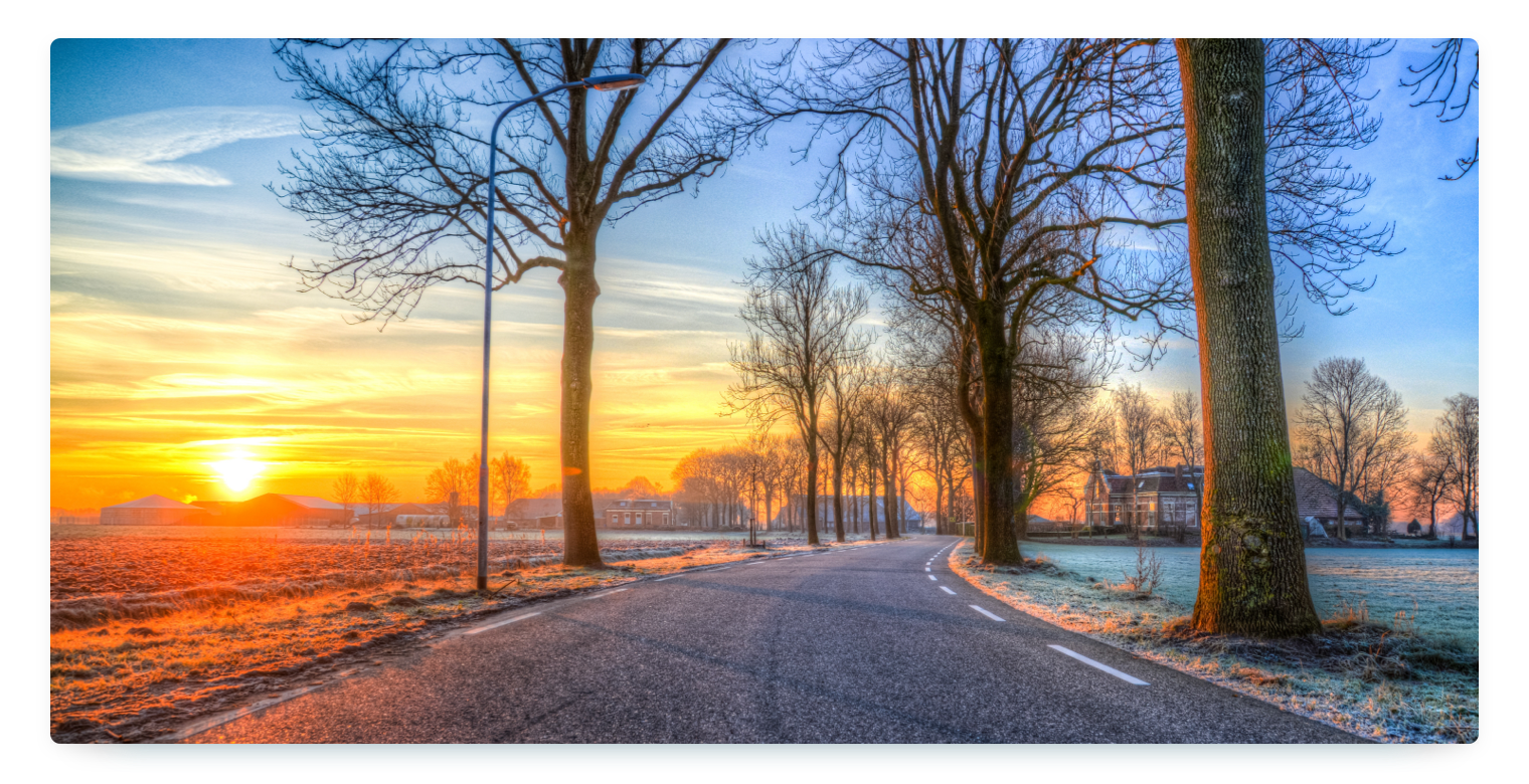 An empty street in winter with trees along the sides and the sun just setting creating a beautiful sky