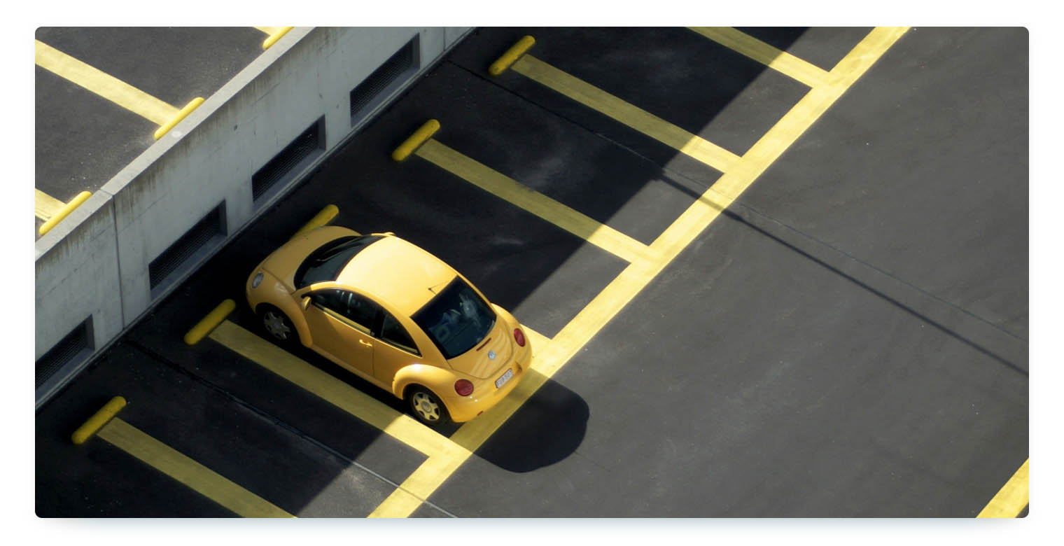 A yellow car is parked on a company parking space that has yellow lines to mark the single spots