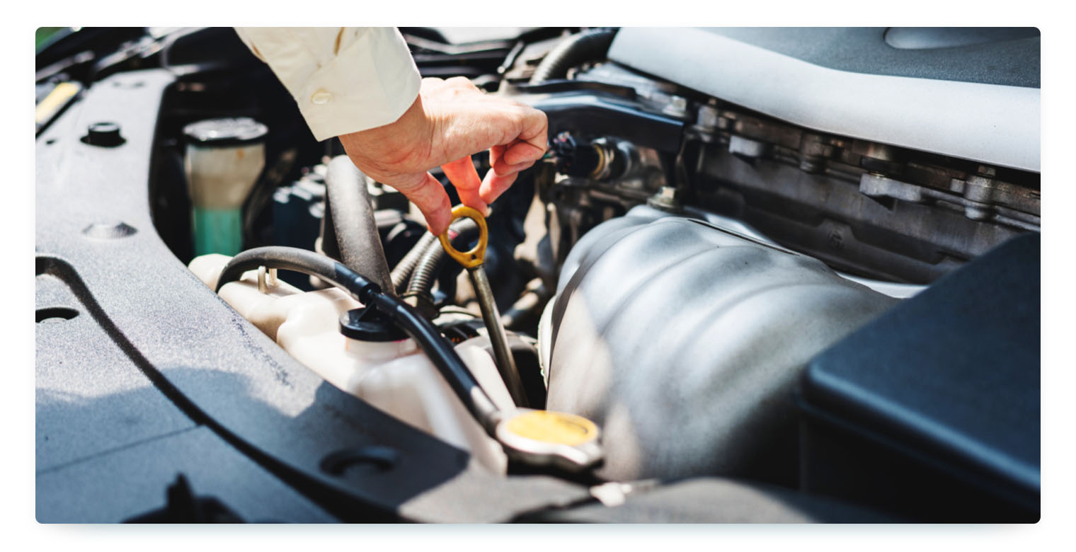 A hand checks the oil level under the hood of a car