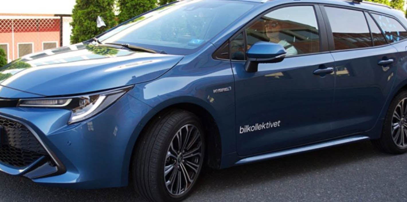 A side view of a blue Toyota hybrid car. The words "bilkollektivet" are written in white text on the car's side door.