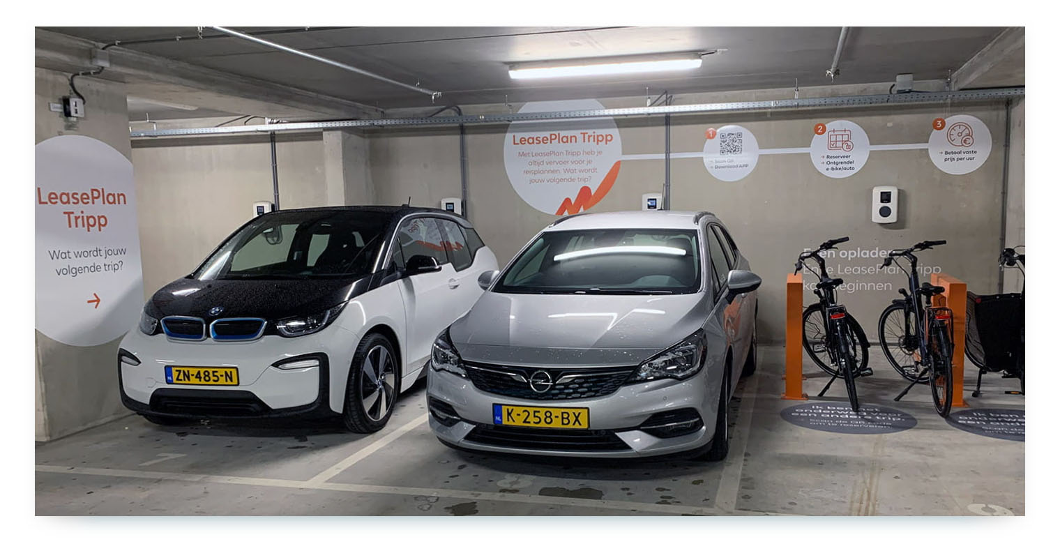 An indoor parking garage shows two shared cars, a BMW i3 and an Opel Astra, from the "LeasePlan Tripp" carsharing service, parked next to two shared bikes.