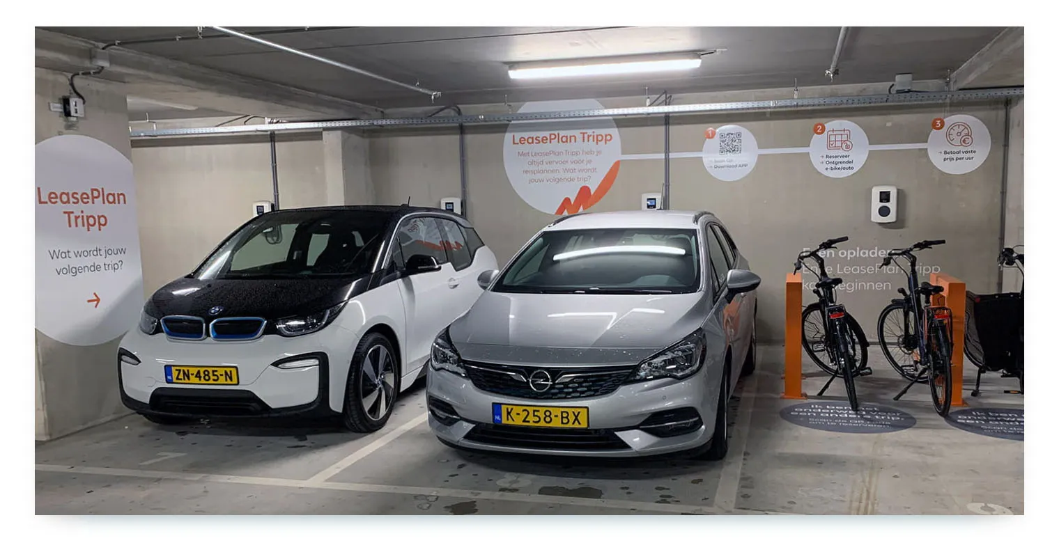 An indoor parking garage shows two shared cars, a BMW i3 and an Opel Astra, from the "LeasePlan Tripp" carsharing service, parked next to two shared bikes.