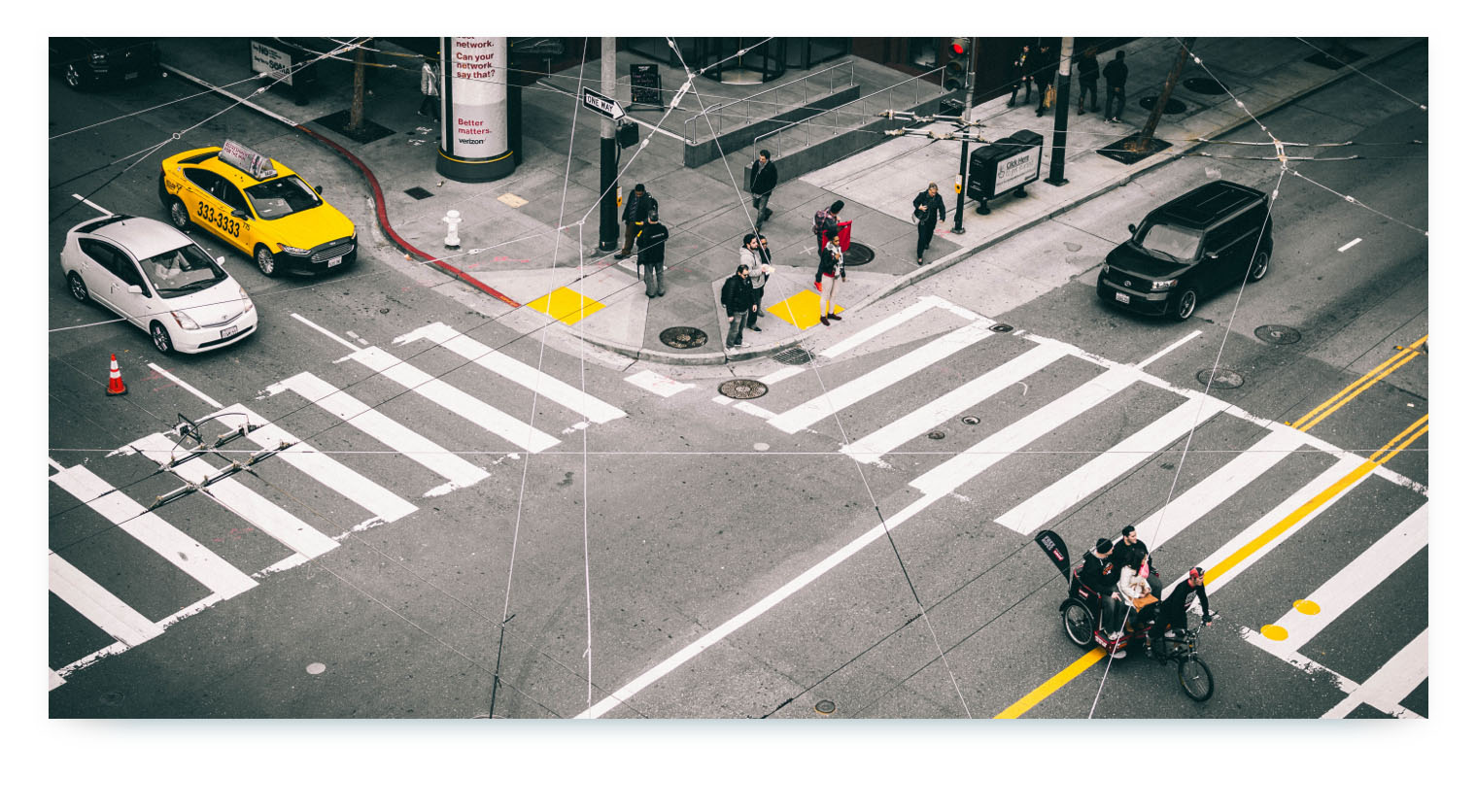 An aerial view of a busy city intersection with pedestrians, a taxi, and other cars. White lines and geometric patterns are digitally superimposed over the image, illustrating the concept of a "smart city" and the interconnectedness of different transport services.