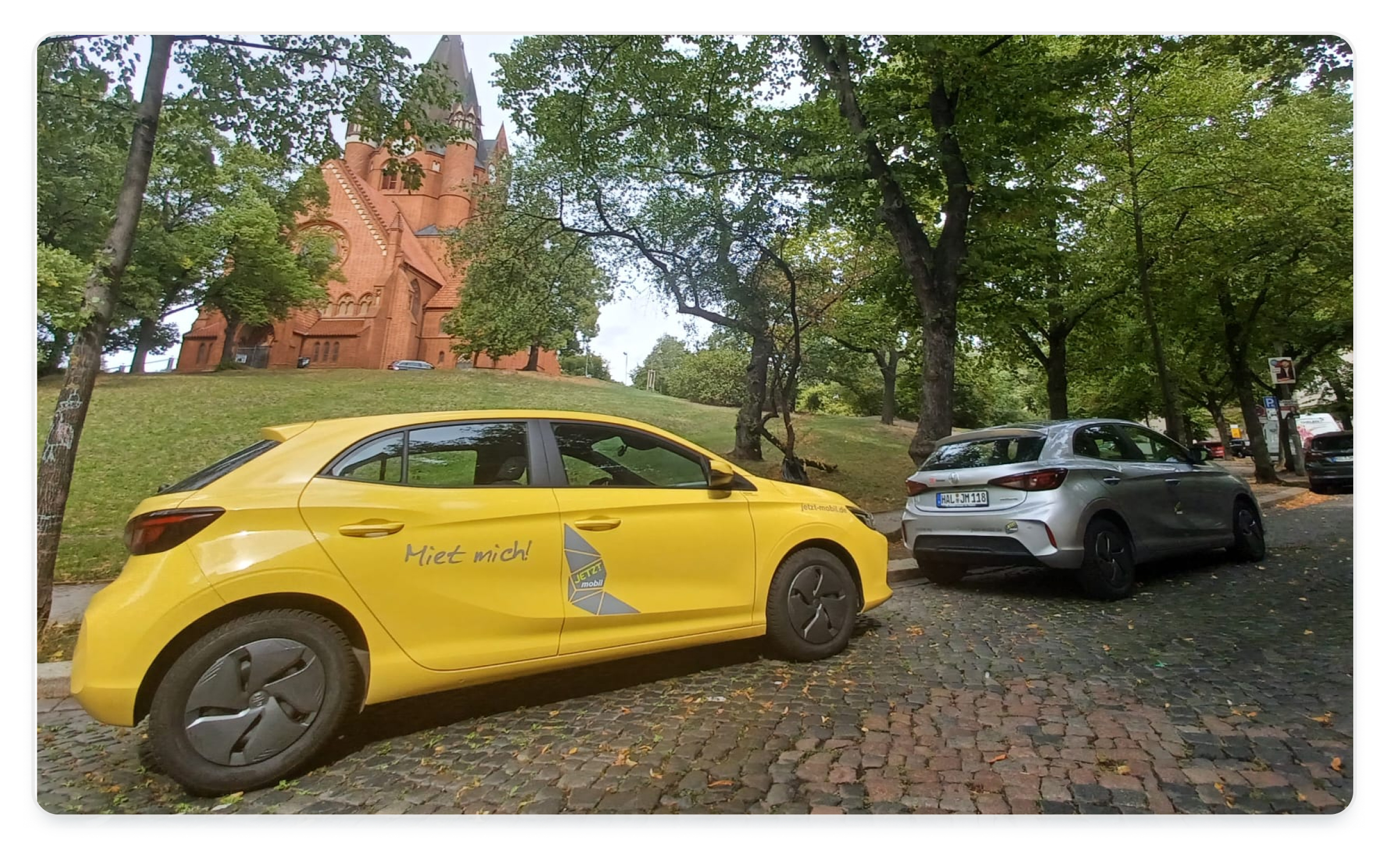 A yellow car sharing car from JETZT mobil is positioned at its station in front of a church in Halle an der Saale