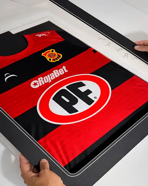 Manos enmarcando camiseta de fútbol rojo y negro con logos de PF y RojaBet.