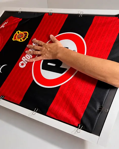 Mano extendida tocando camiseta roja y negra del Club Deportivo O'Higgins enmarcada en la pared.