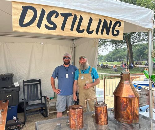 Image of two people standing and smiling behind an alcohol still.