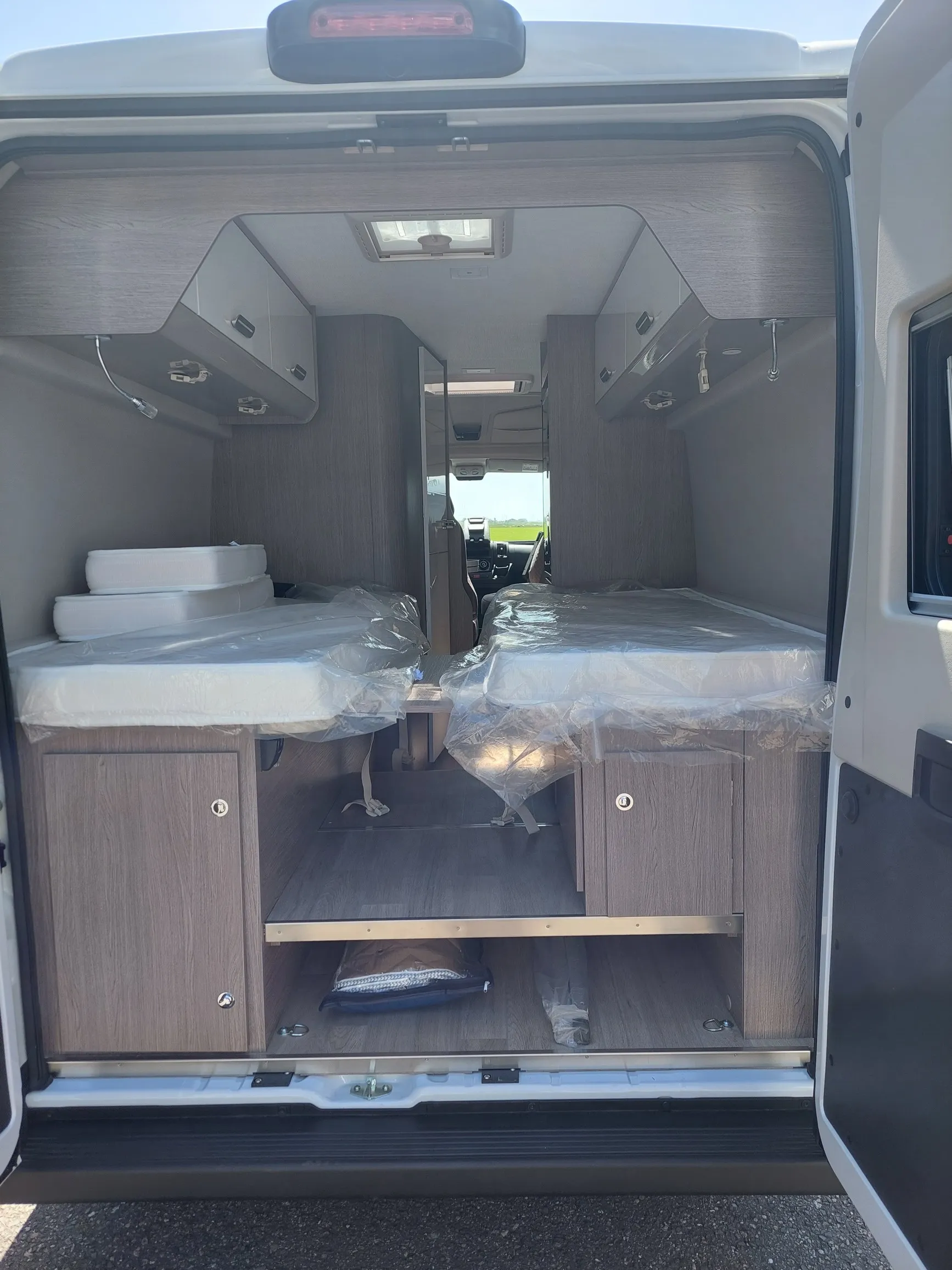 Interieur van een Chausson V217 met twee bedden bedekt met plastic en opbergruimte eronder.
