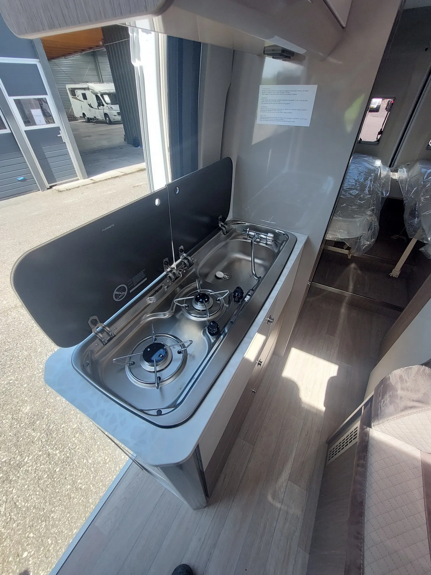 Compact keukengedeelte van de Chausson V217 met een ingebouwde gasfornuis en spoelbak in een camper met plastic beddengoed zichtbaar in de achtergrond.