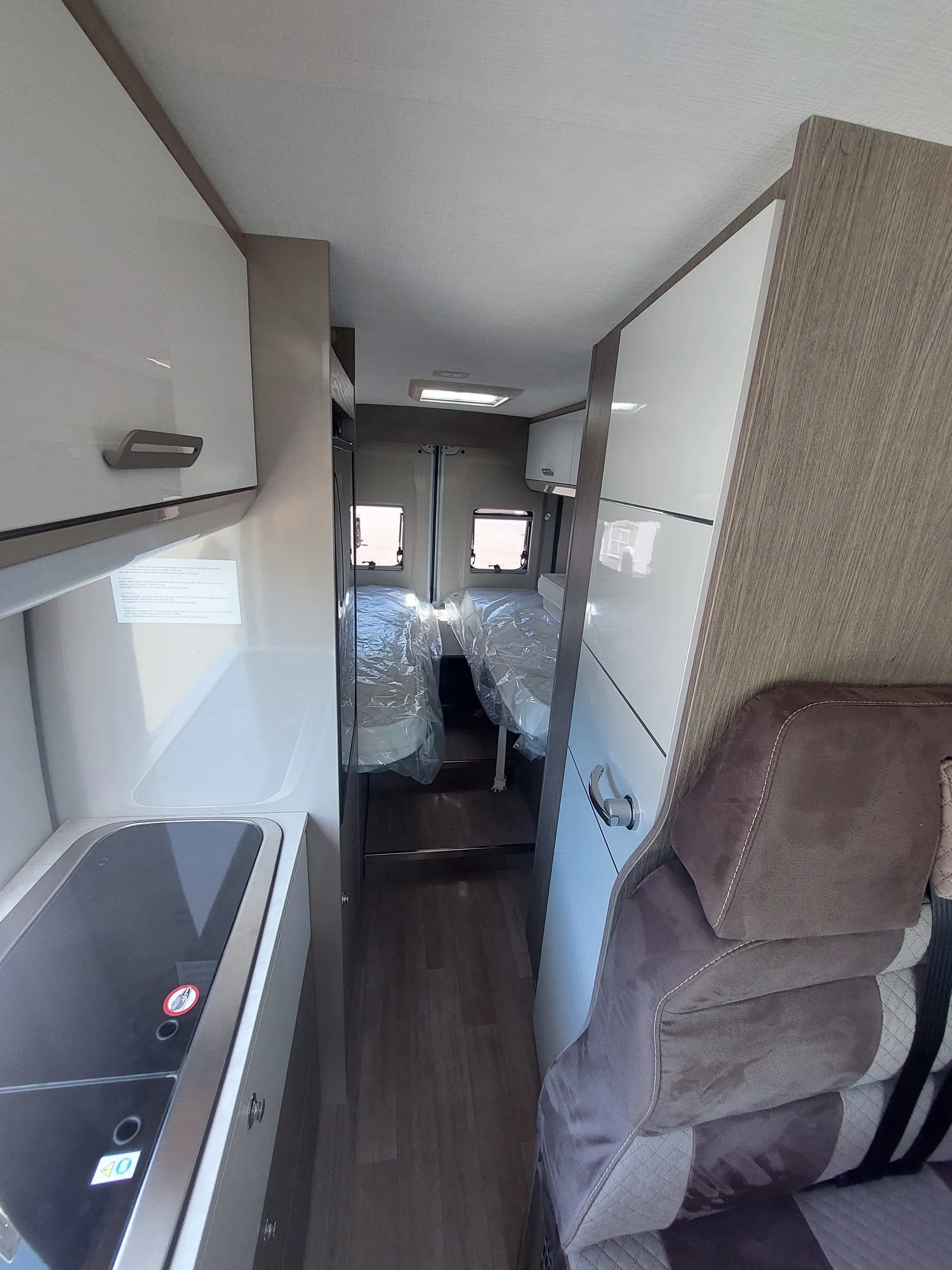 Binnenaanzicht van de Chausson V217 met een kleine keukenlinks, gang en twee bedden aan de achterkant bedekt met plastic.