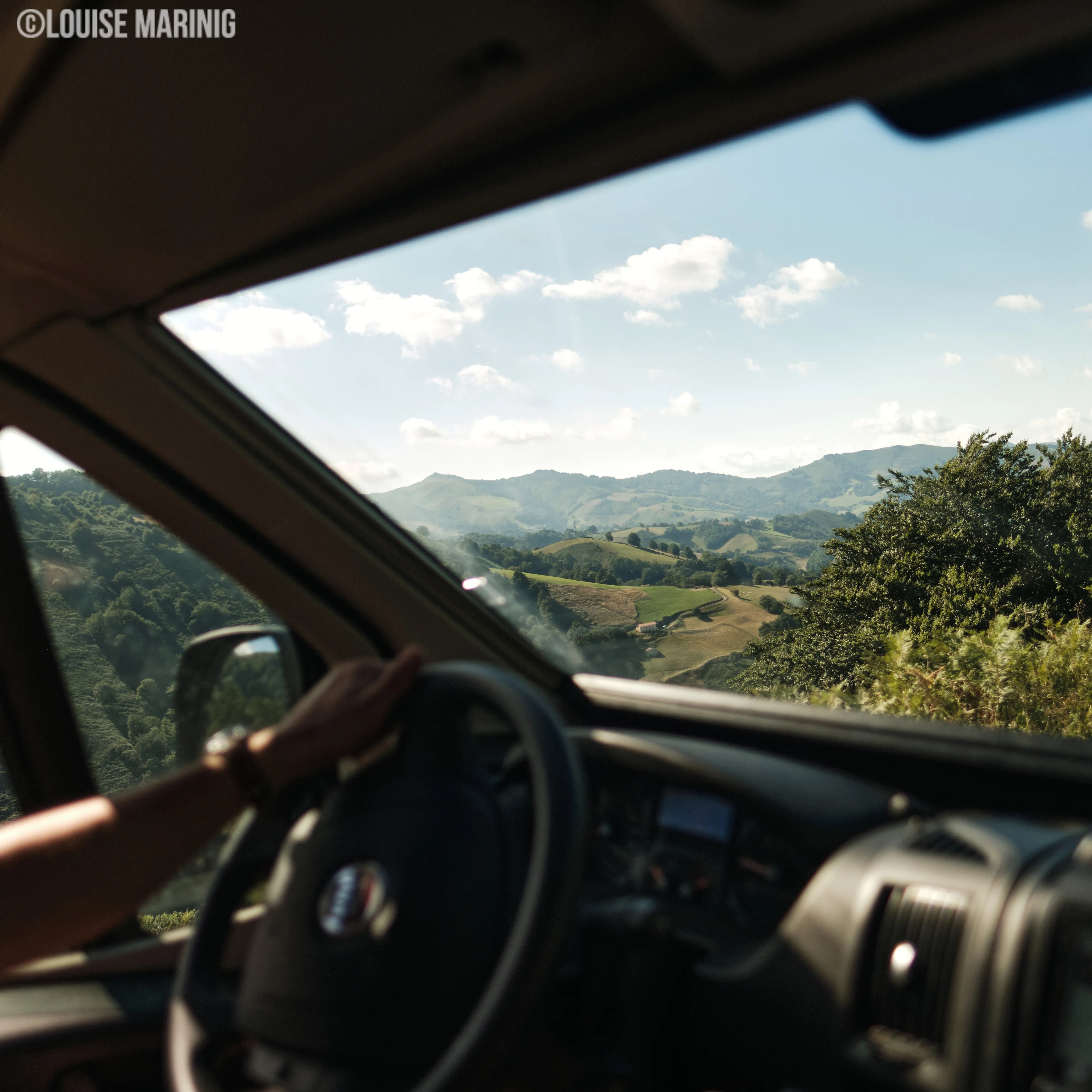 Uitzicht vanuit een Chausson camper op een landschap met groene heuvels en een blauwe lucht met wolken.