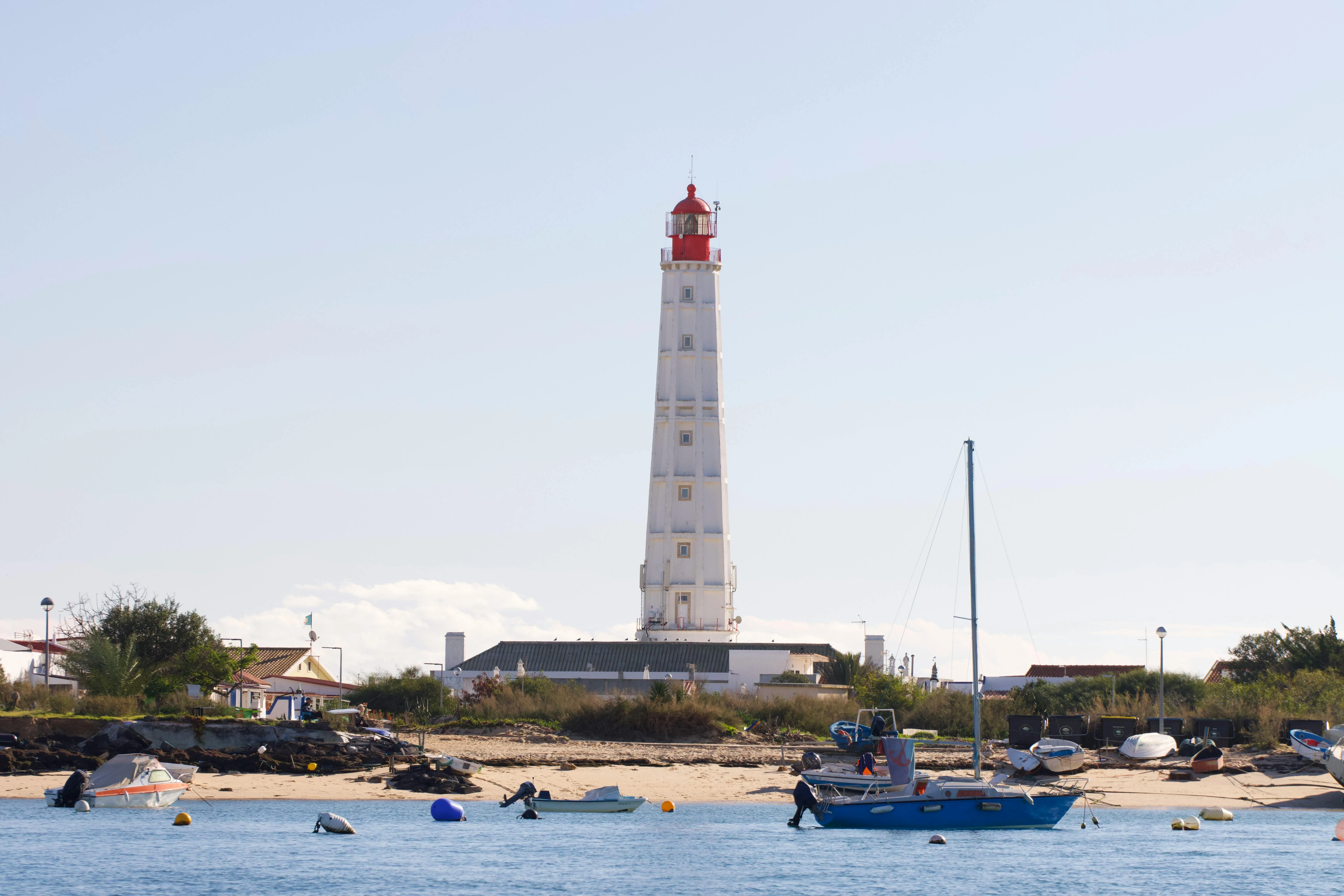 Vuurtoren met een rode top aan een kustlijn met boten in het water en een zandstrand.