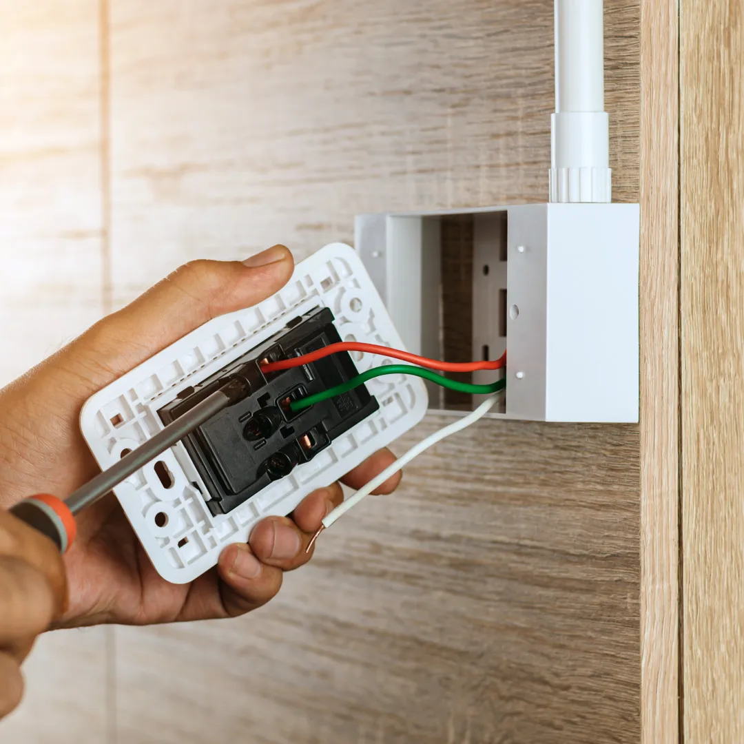 Nahaufnahme der Hand eines Elektrikers, der eine Steckdose mit einem Schraubendreher an einer Wand installiert.