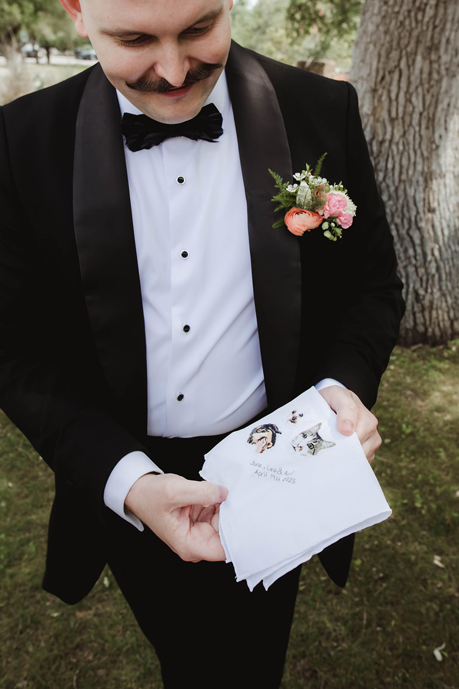 The groom holding a custom embroidered handkerchief of their three pets and the date of their wedding.