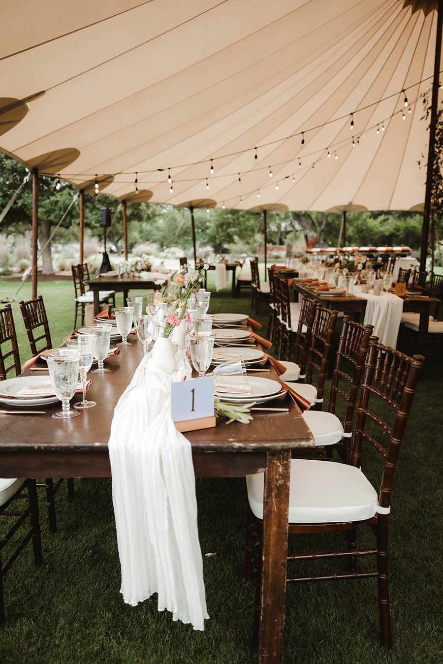 A display of the table numbers on wooden tables under a tent for a wedding dinner.