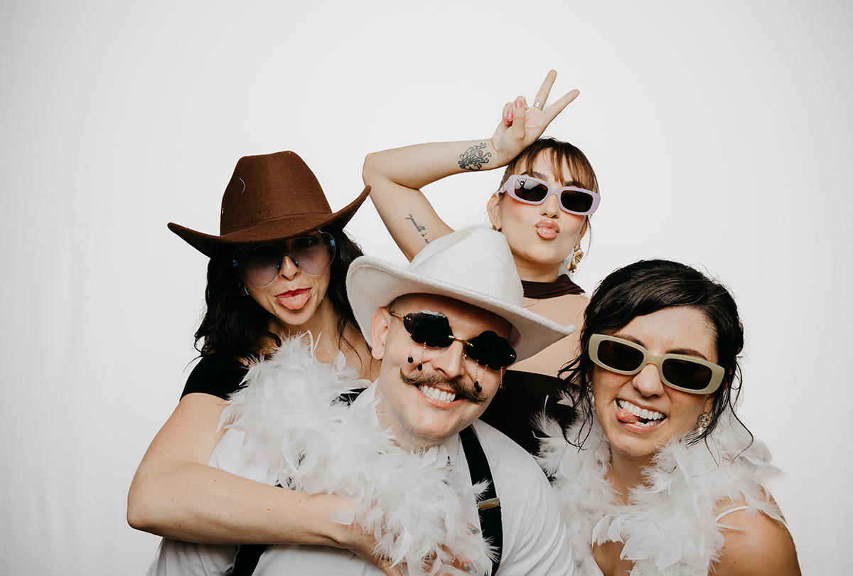 Four people pose with props on a white background. 
