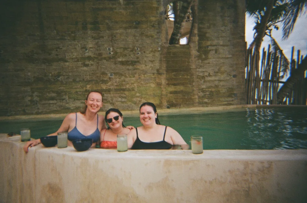 Three friends swimming in a pool posing for the camera.