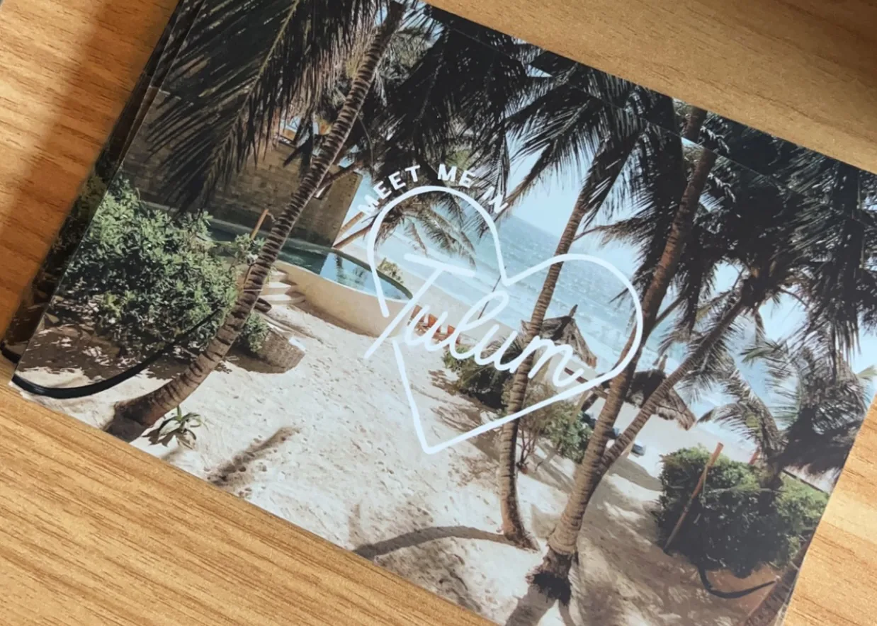Invitation postcard on a desk with a photo of the Tulum beach with the "Meet me in Tulum" logo
