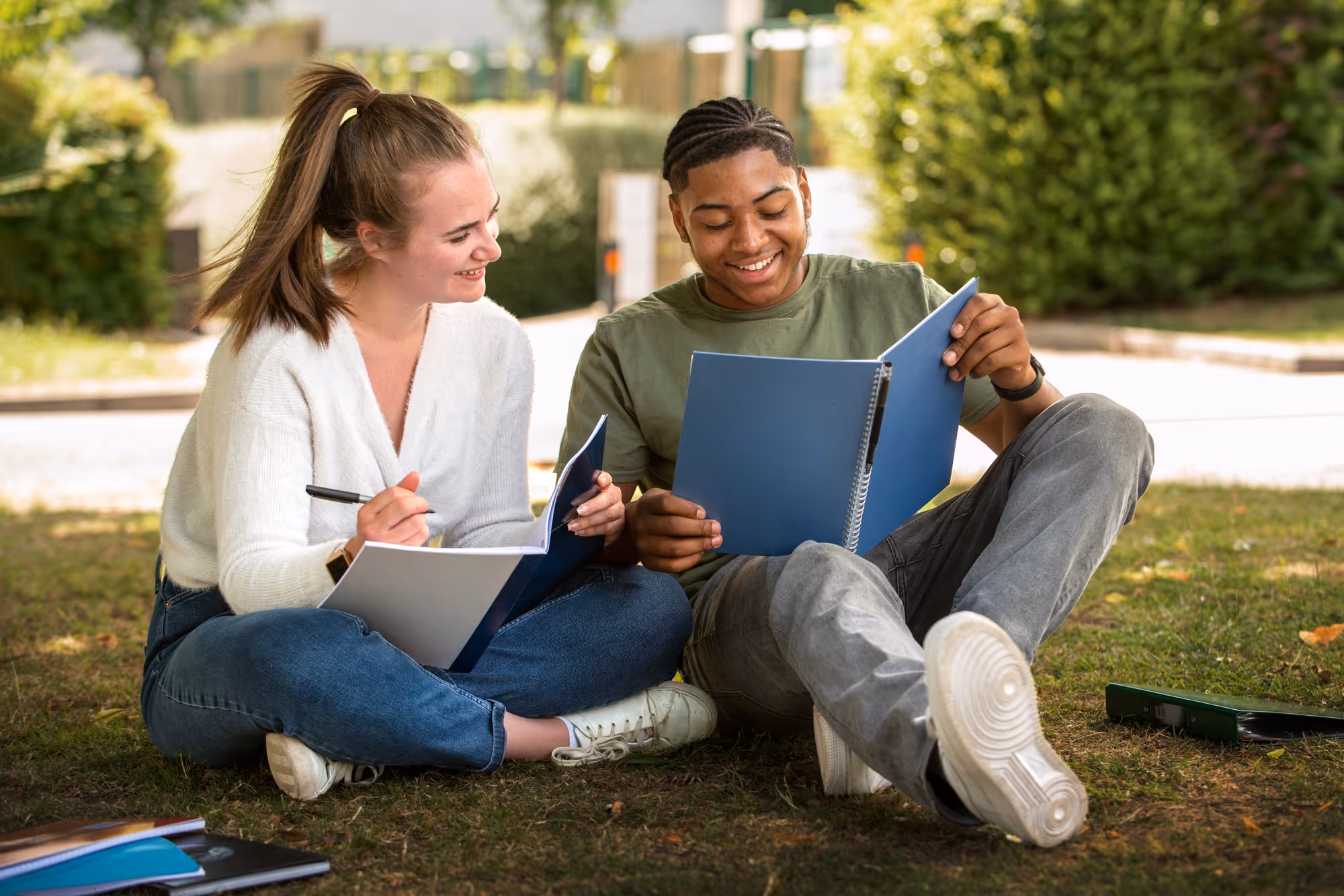 Two students sitting on grass, reviewing insurance-related documents for their studies in Germany