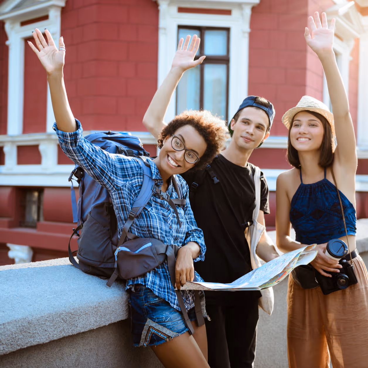 Three young people with backpack, camera, and map smiling in front of a red building