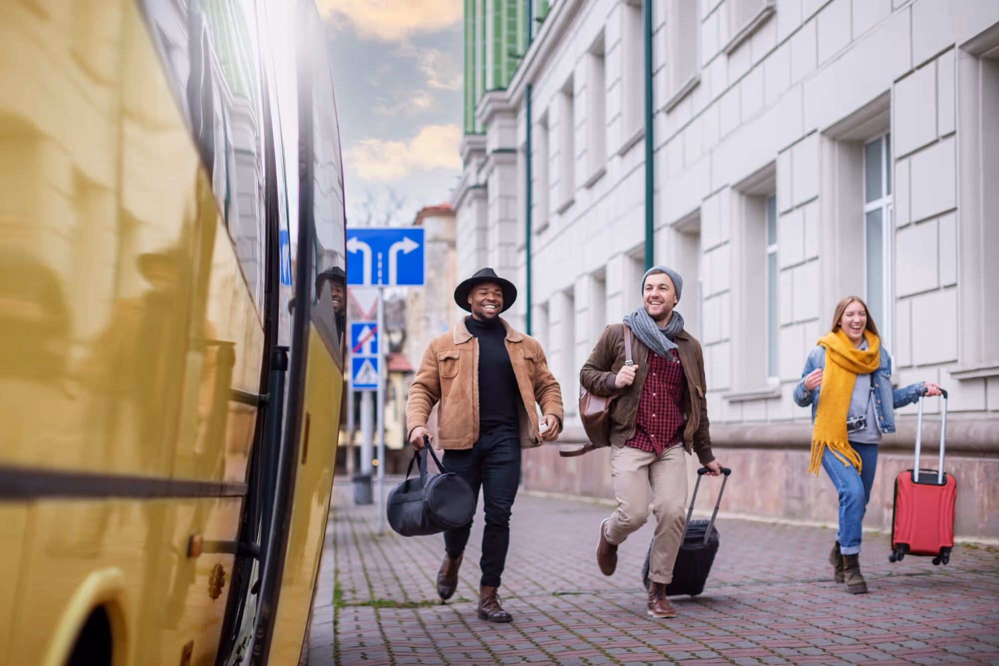 Group of international students joyfully arriving with luggage near a yellow bus