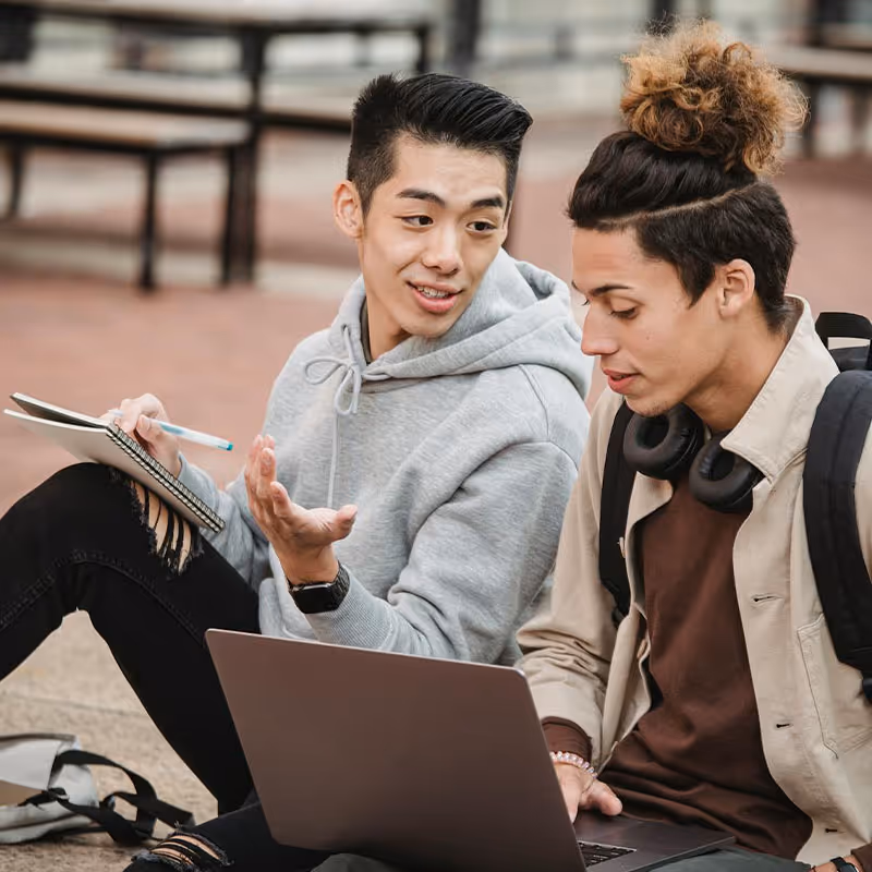 Two students talking and looking at a laptop