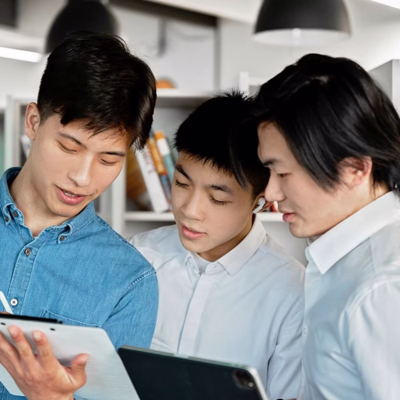 Three young men collaborating in an office, looking at digital tablets together.