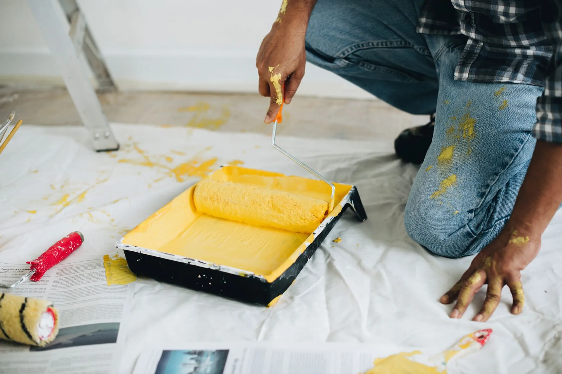 Person beim Streichen mit gelber Farbe – Nahaufnahme einer Hand mit Farbroller auf Malerfolie. Symbolbild für professionelle Malerarbeiten.