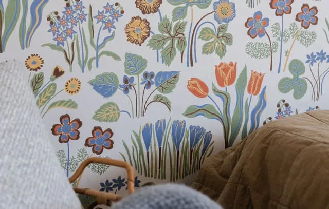 Nahaufnahme einer Schlafzimmerwand mit einer bunten Blumentapete und einem Teil eines Bettes.