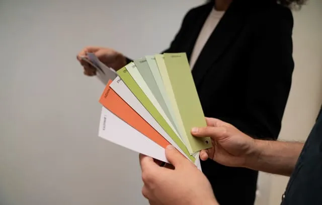 Zwei Personen, die gemeinsam Farbmusterkarten in verschiedenen Grün-, Orange- und Beigetönen auswählen.