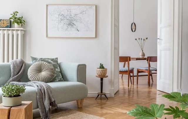 Stilvolles Wohnzimmer mit hellblauer Couch, Holzboden und einer offenen Tür, die den Blick auf ein Esszimmer freigibt.
