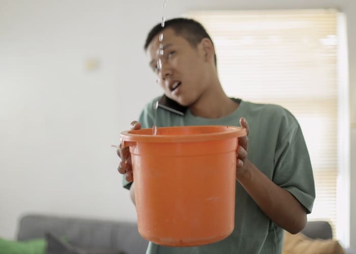a man with a bucket collection leaking water from the ceiling