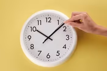 a clock with a hand pinching it on the yellow wall