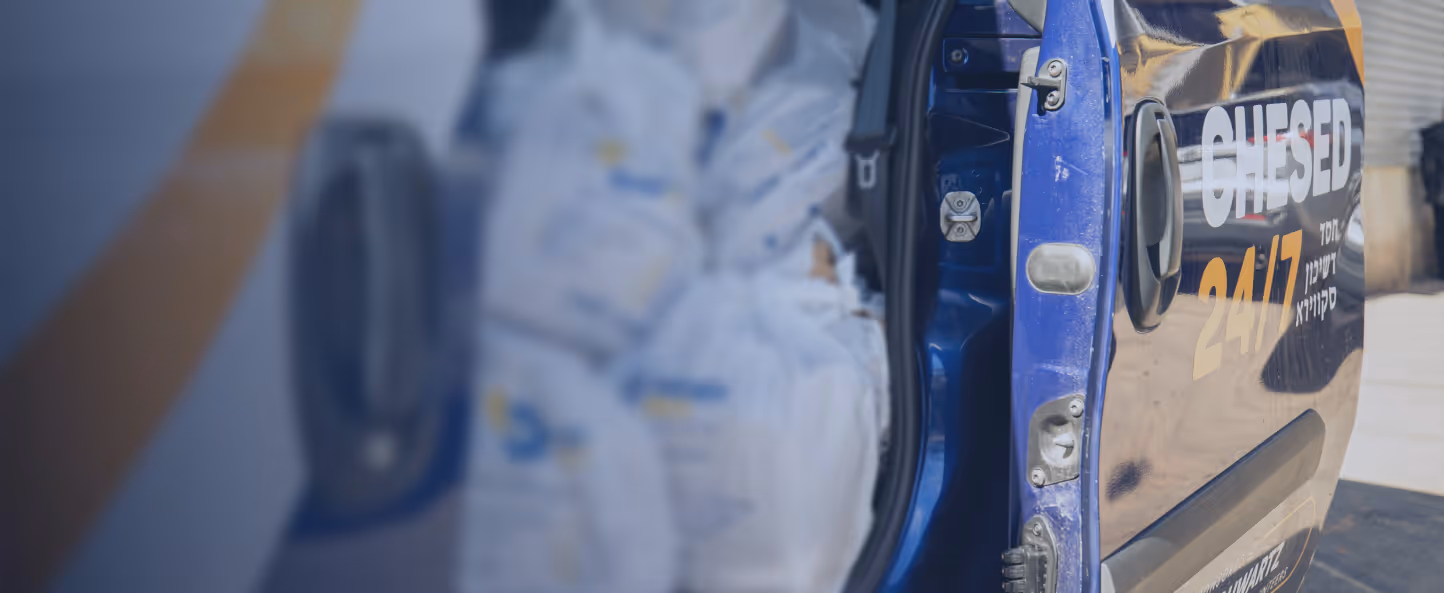 Open door of a blue van with 'CHESED 24/7' text, showing stacked white bags inside.