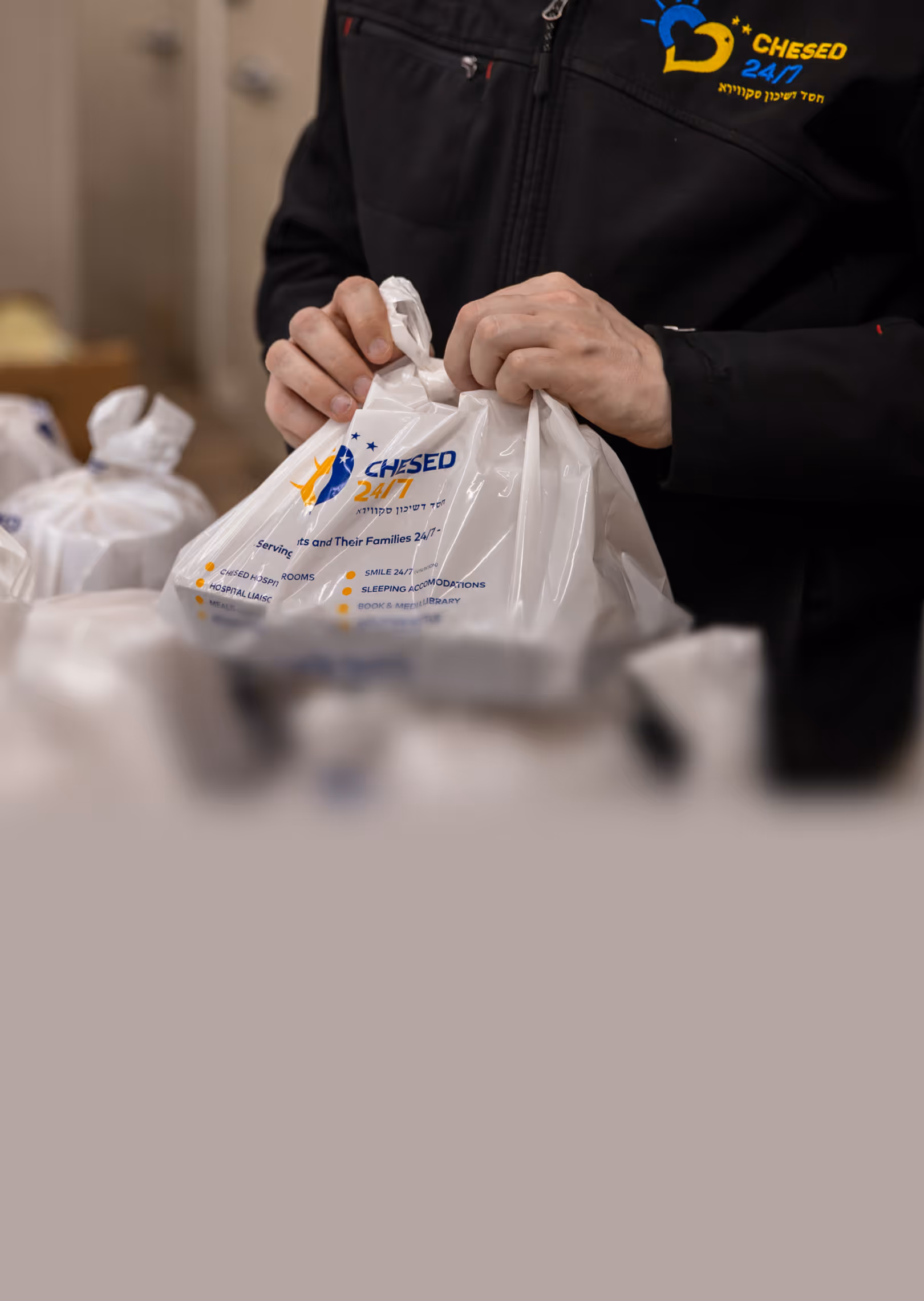 Person tying the top of a white plastic bag with Chesed 24/7 logo and service details printed on it.