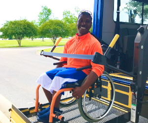 Passenger in wheelchair using assist technology to board bus.