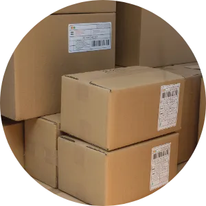 Stack of plain brown cardboard boxes with white shipping labels, arranged inside a larger box or container against a plain background.