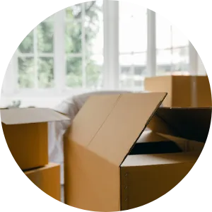 Stack of open and closed cardboard boxes in a bright room with large windows, suggesting packing or moving activity.