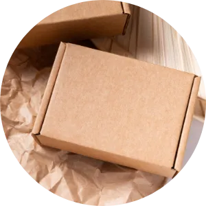 Plain brown cardboard box resting on crumpled brown packing paper with parts of other similar boxes in the background.