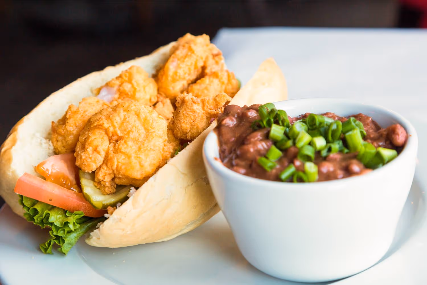 A sandwich with shrimp and a bowl of beans.