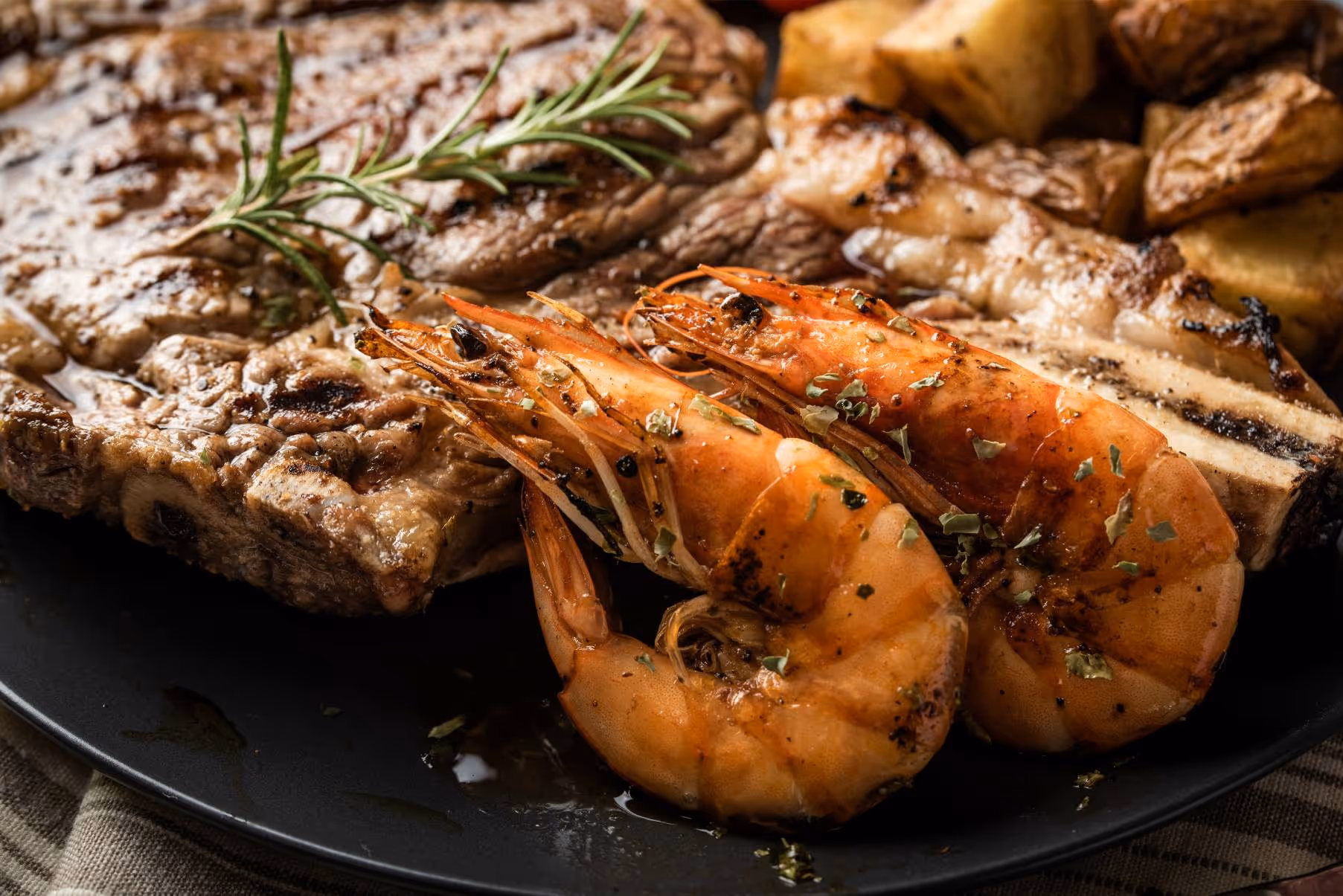 A plate of shrimp and steak with herbs on top.