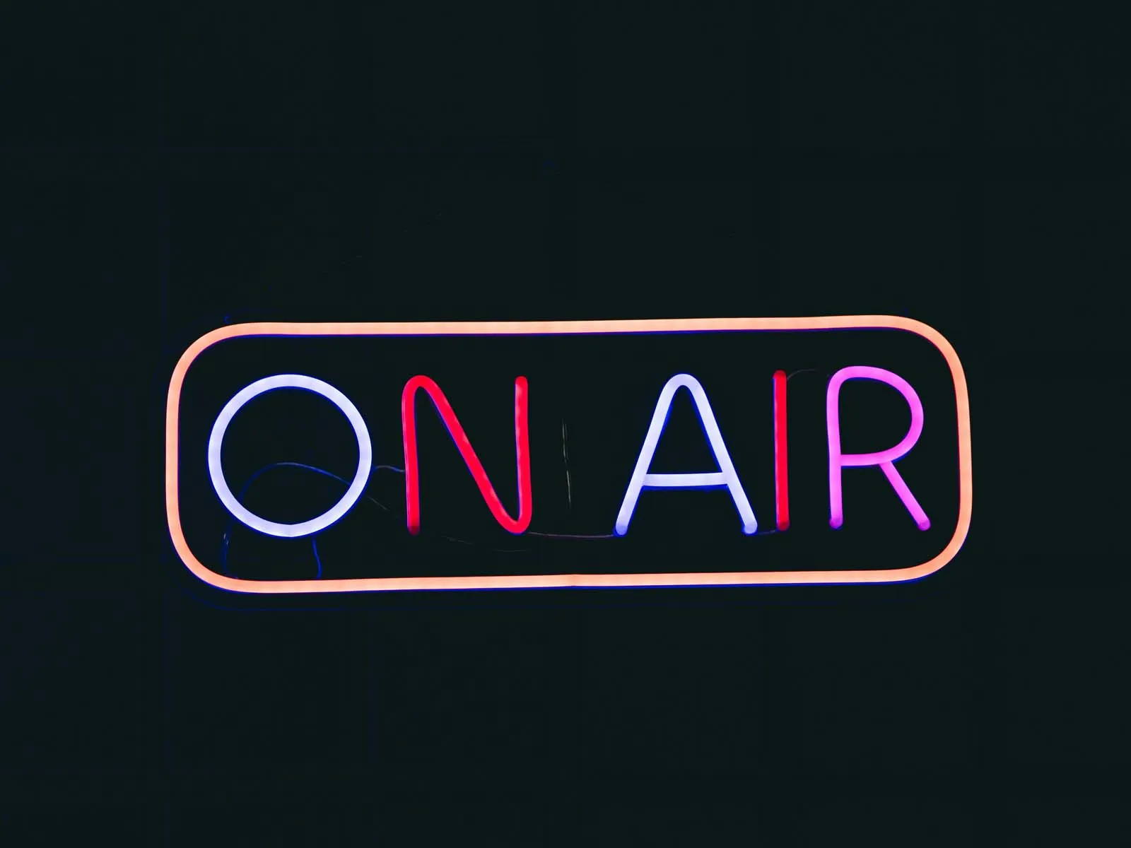 Neon “ON AIR” sign glowing in blue, red, and purple against a black background.
