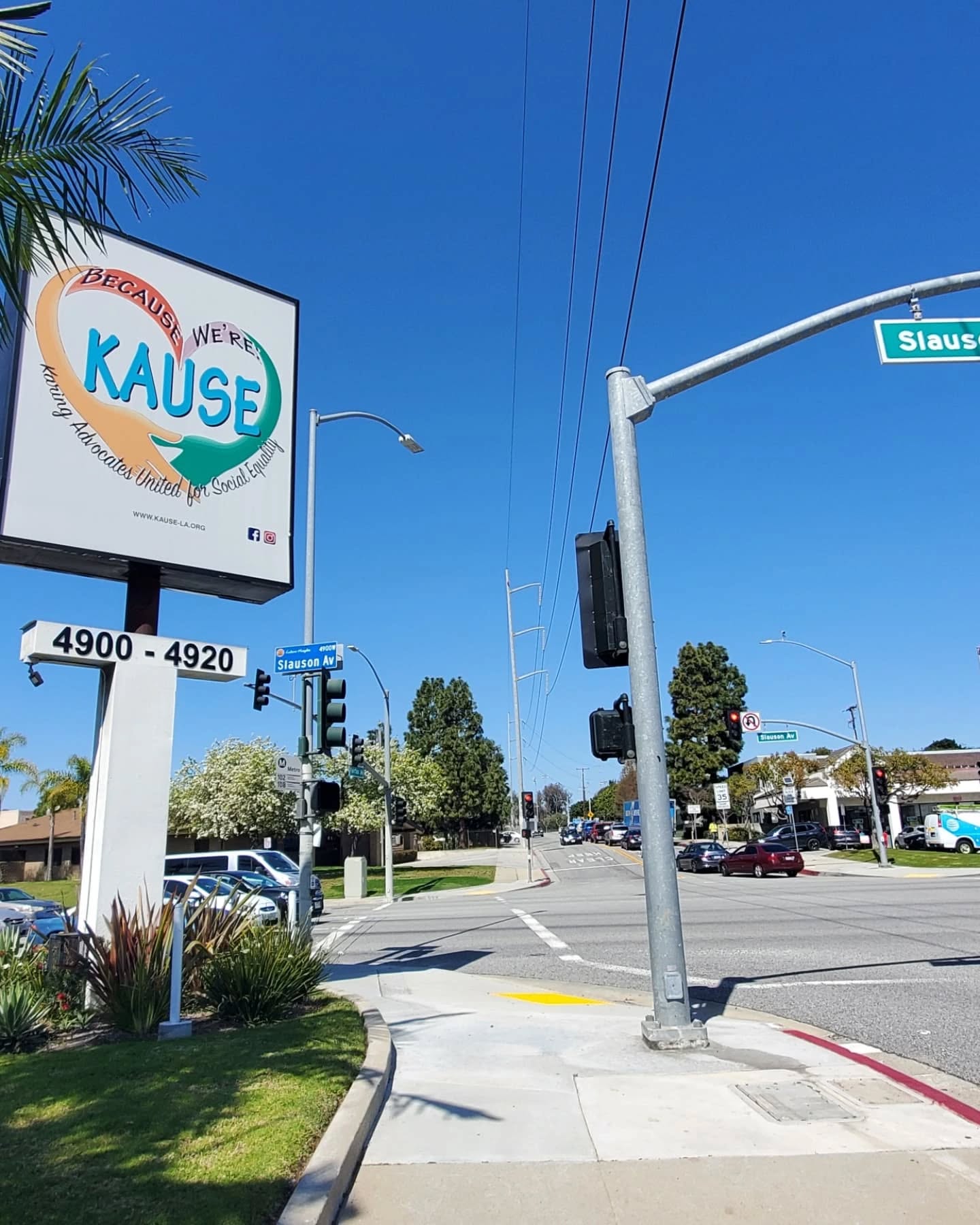 Street corner view showing a large sign for KAUSE nonprofit, with the slogan 'Keeping Advocates United for Social Equity' on a clear sunny day in Los Angeles.