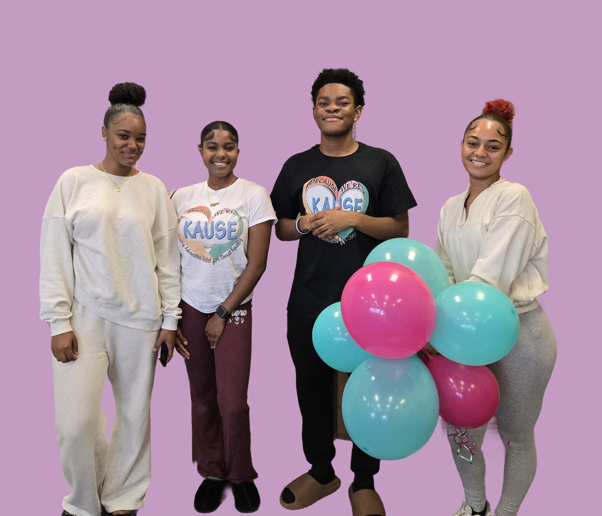 Group of four smiling young adults standing together in casual clothing, with one holding teal and pink balloons, in front of a solid lavender background.