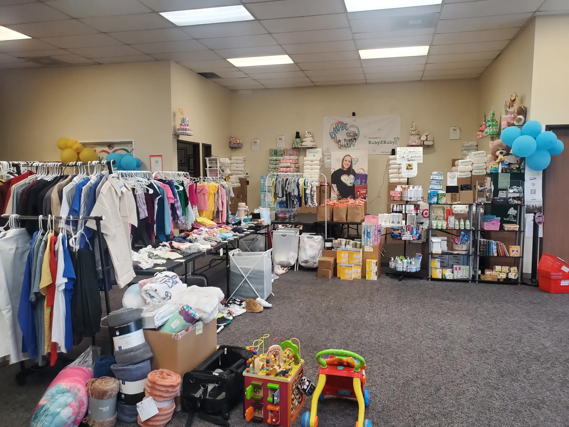 Community donation room filled with baby and children's clothes, toys, and essential supplies neatly organized on racks and shelves.